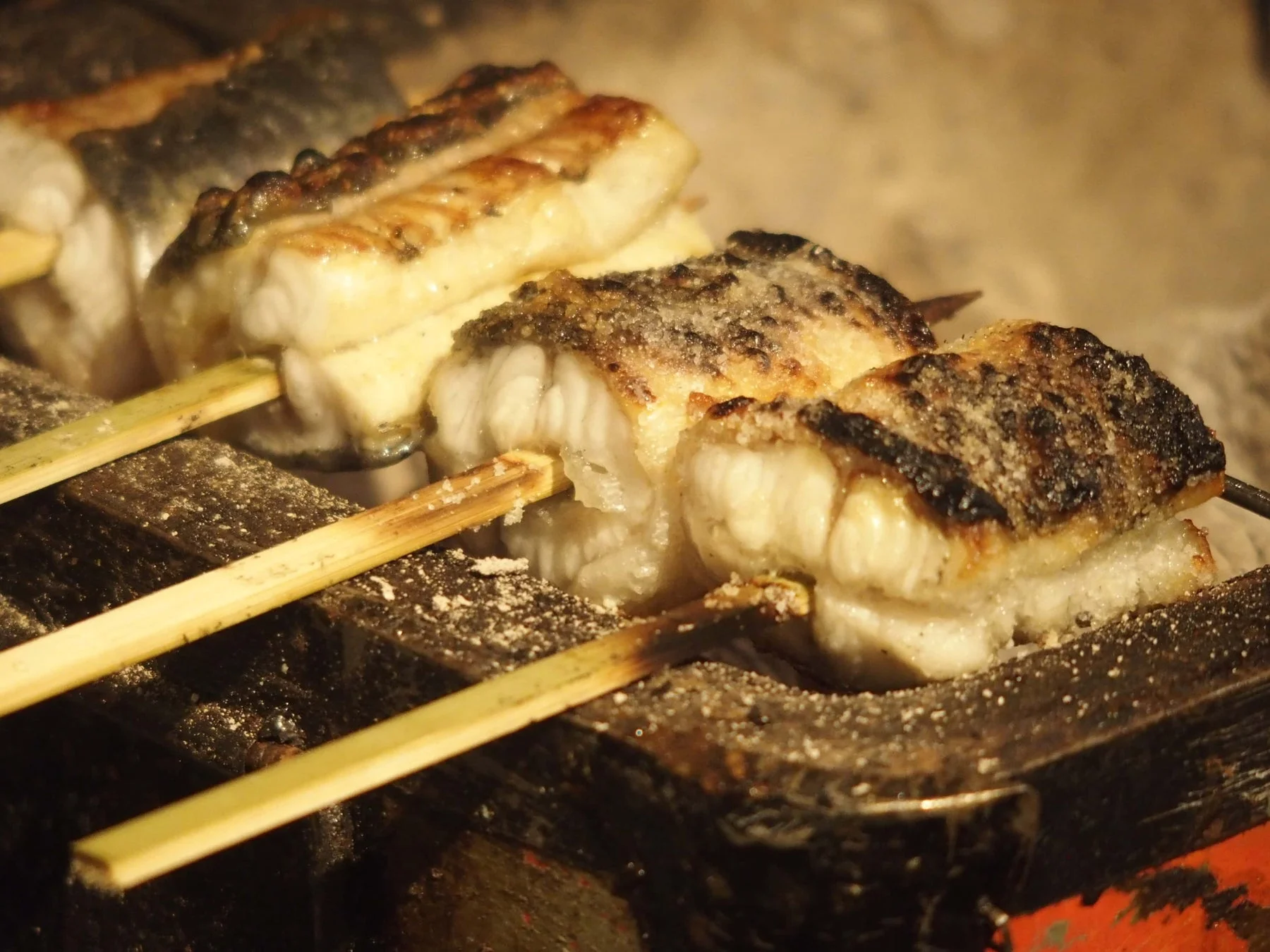 炭火で焼かれる串刺しの魚